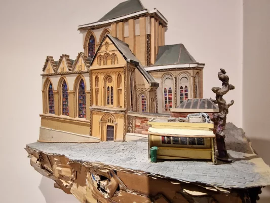 “Friture de la Chapelle” (lijm, karton en diverse materialen, 2017, collectie Home Frit’ Home) van Yorick Efira vat in maquettevorm het typisch Belgische gebaar samen waarbij een frietkraam letterlijk tegen een monumentale heilige plek wordt aangebouwd: hier warmt Friture de la Chapelle in alle seizoenen de parochiekerk Onze‑Lieve‑Vrouw ter Kapelle (Brussel) op. Friture-Chapelle_Yorick-Efira_WEBP
